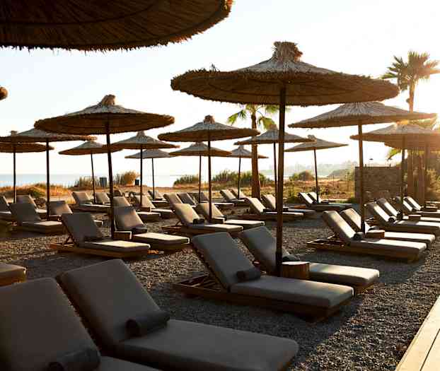 Rivi aurinkotuoleja ja aurinkovarjoja kivisellä rannalla, taustalla meri. (Tekoälyn luoma teksti)