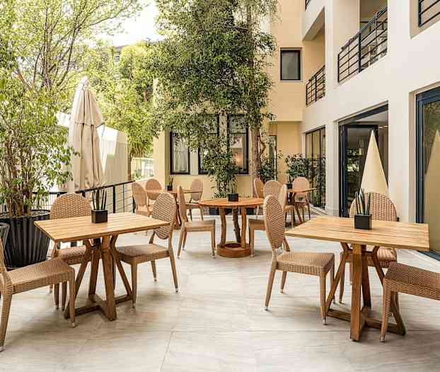 Ulkotila, jossa pöytiä ja tuoleja kasvien ympäröimänä. (Tekoälyn luoma teksti)