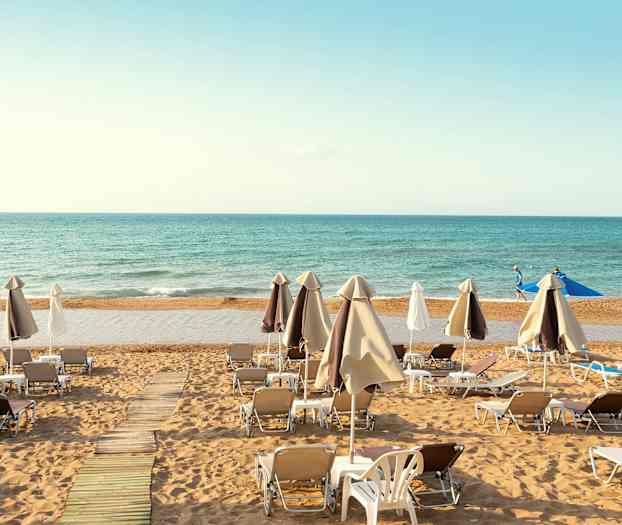 Aurinkotuoleja ja aurinkovarjoja asetettu hiekkarannalle, taustalla meri. (Tekoälyn luoma teksti)