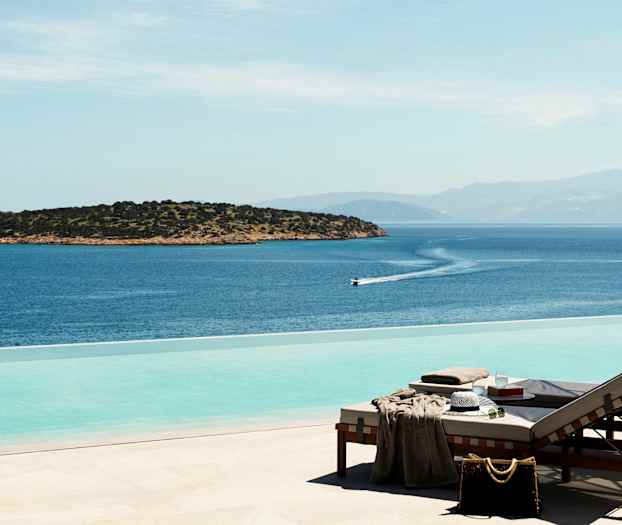 Aurinkotuoleja infinity-altaan äärellä, josta on näkymä merelle ja pienelle saarelle. (Tekoälyn luoma teksti)