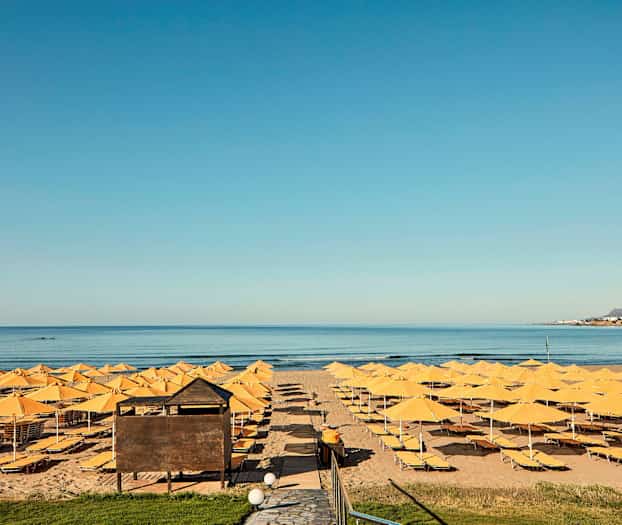 Ranta, jossa on keltaisia aurinkovarjoja ja aurinkotuoleja meren edessä. (Tekoälyn luoma teksti)