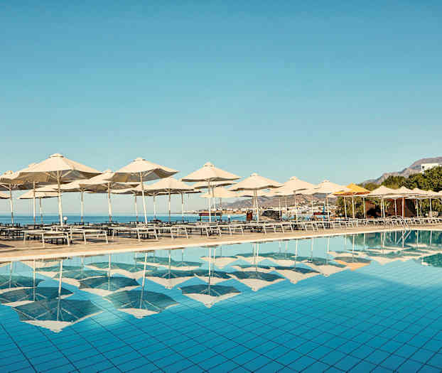 Aurinkotuoleja ja varjoja altaan vieressä, näkymä merelle. (Tekoälyn luoma teksti)