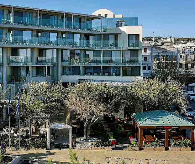 Moderni hotelli, jossa on parvekkeita ja ulkona sijaitseva istuinalue katoksen alla sekä taivasalla, ympäröitynä puilla. (Tekoälyn luoma teksti)