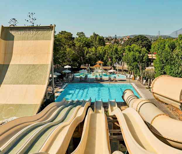 Kuva vesipuistosta, jossa on useita vesiliukumäkiä, jotka johtavat altaaseen, jota ympäröivät vihreät puut. (Tekoälyn luoma teksti)