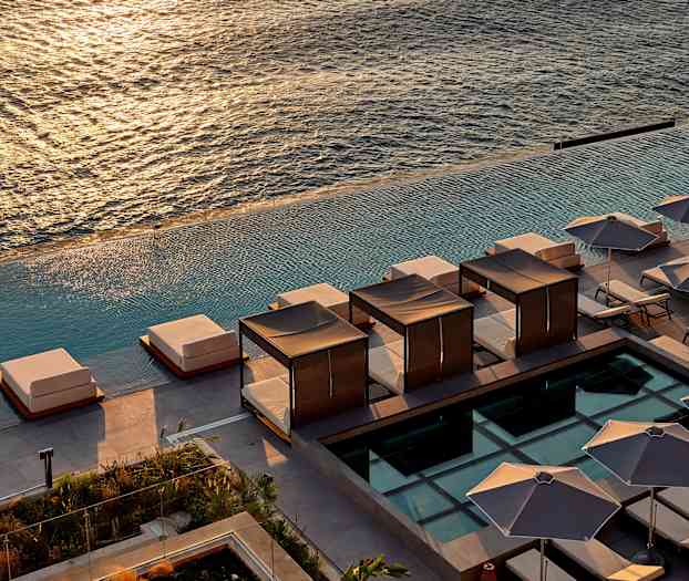 Näkymä aurinkotuoleista ja varjostavista aurinkovarjoista infinityaltaan reunalla, taustalla näkyy meri. (Tekoälyn luoma teksti)