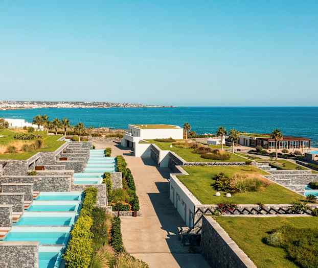 Näkymä lomakeskuksesta meren rannalla yksityisillä uima-altailla ja vehreillä alueilla. (Tekoälyn luoma teksti)