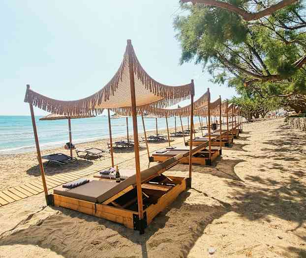 Kuva hiekkarannasta, jossa on aurinkotuoleja ja puuvarjostimia. (Tekoälyn luoma teksti)