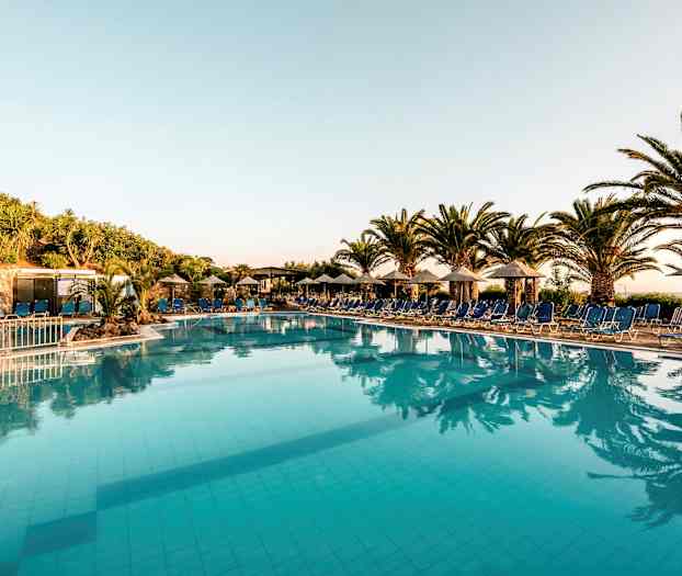 Ulkoilmauima-allas, jota ympäröivät aurinkotuolit ja varjot, taustalla palmuja ja kasvillisuutta. (Tekoälyn luoma teksti)