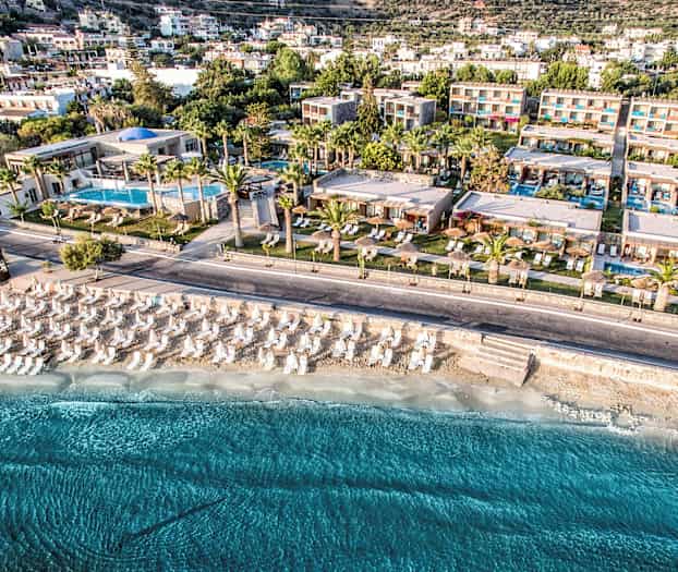 Ilmakuva lomakohteesta rannalla, jossa on aurinkovarjoja ja aurinkotuoleja. (Tekoälyn luoma teksti)