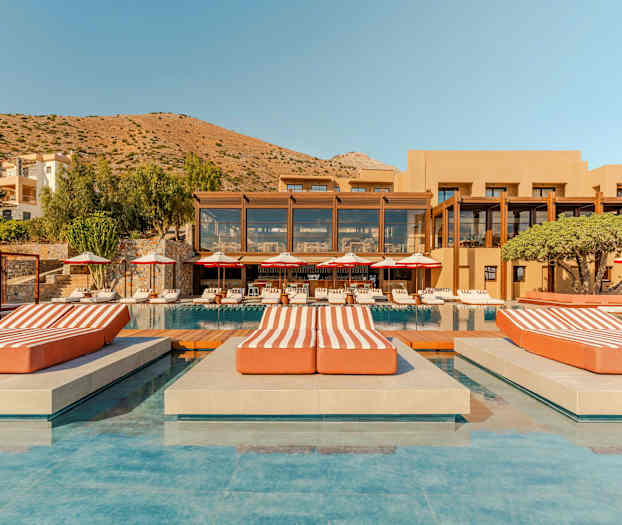 Ylellinen hotellikompleksi, jossa uima-allas, aurinkotuoleja ja vuoristoinen tausta. (Tekoälyn luoma teksti)