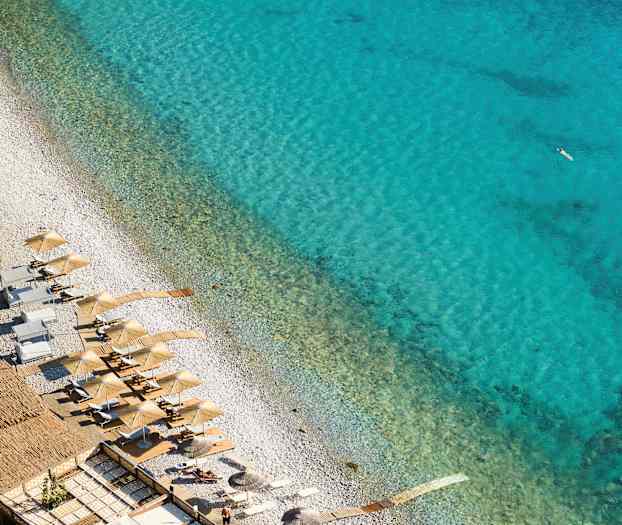 Näkymä rannalle, jossa on aurinkovarjoja ja aurinkotuoleja kirkkaan sinisen veden äärellä. (Tekoälyn luoma teksti)