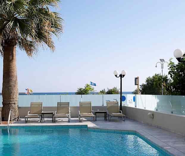 Uima-allas, jonka vieressä aurinkotuoleja ja pöytä, ympärillä lasiseinät. Puita ja näkymä merelle taustalla. (Tekoälyn luoma teksti)