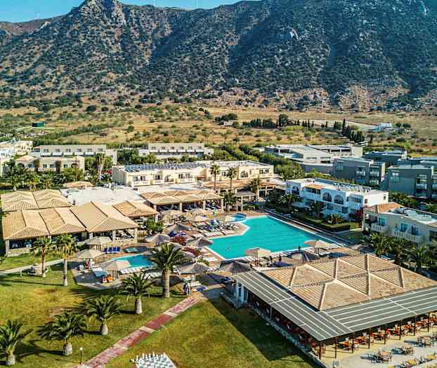 Kuva lomahotellista, jossa on uima-allas ja ympäröiviä rakennuksia, sijaiten lähellä vuoristomaisemaa. (Tekoälyn luoma teksti)