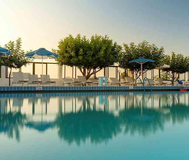 Ulkouima-allas, jota ympäröivät puut, aurinkovarjot ja aurinkotuolit. (Tekoälyn luoma teksti)