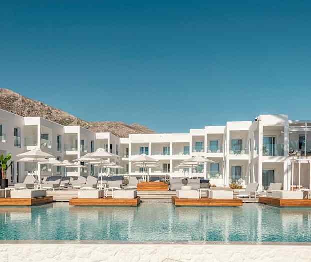 Valkoinen hotellirakennus, jossa on ulkouima-allas ja aurinkotuoleja. (Tekoälyn luoma teksti)