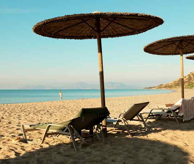 Hiekkaranta, jossa aurinkovarjoja ja aurinkotuoleja meren rannalla. (Tekoälyn luoma teksti)