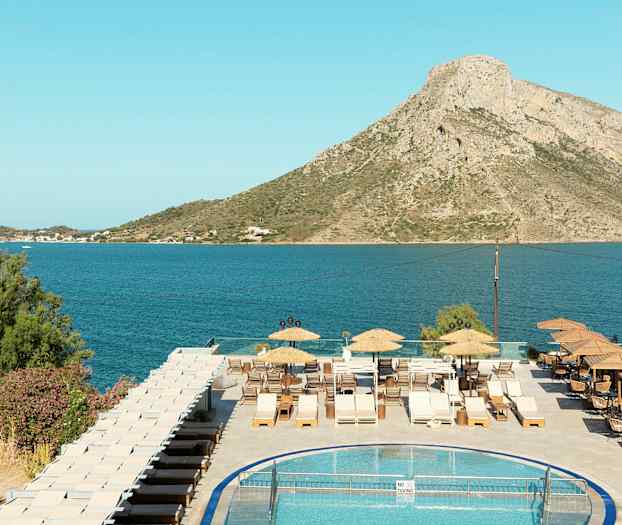 Näkymä uima-altaalle, terassille aurinkotuoleineen ja merimaisemaan, taustalla vuori. (Tekoälyn luoma teksti)