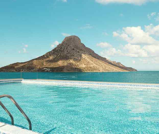 Uima-allas, jossa kirkasta sinistä vettä vuoren edessä meren äärellä kirkkaan taivaan alla. (Tekoälyn luoma teksti)