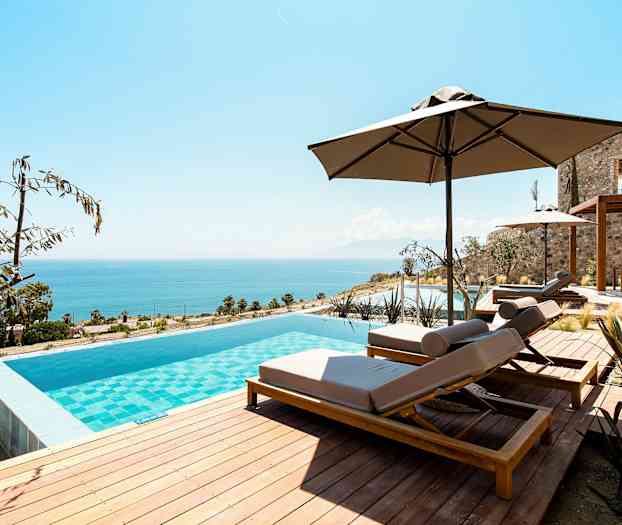 Äärettömyysallas aurinkotuoleilla ja varjoilla, taustalla näkyy meri. (Tekoälyn luoma teksti)