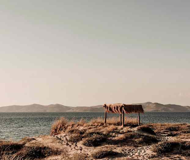 Rantamaisema, jossa yksinkertainen puusta ja oljesta tehty suoja meren äärellä. (Tekoälyn luoma teksti)