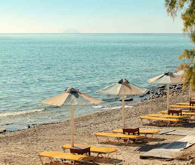 Aurinkotuoleja ja aurinkovarjoja hiekkarannalla, näkymä merelle. (Tekoälyn luoma teksti)