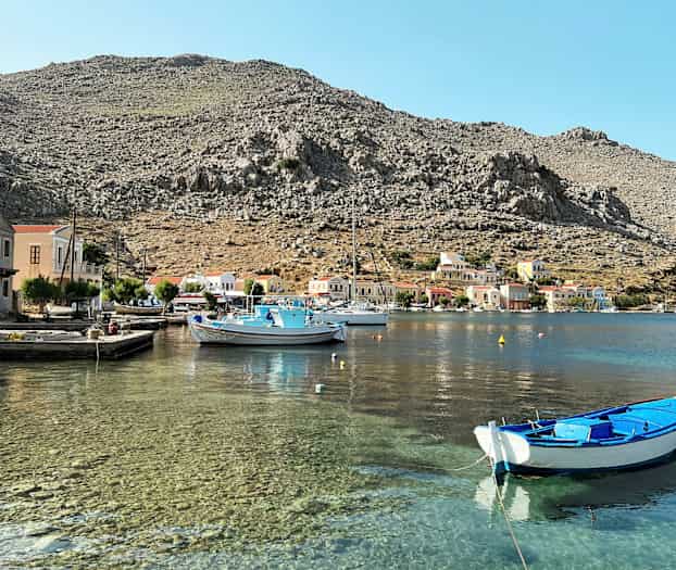 Satama kirkkaalla vedellä, pieniä veneitä ja värikkäitä taloja kivisten vuorten juurella. (Tekoälyn luoma teksti)