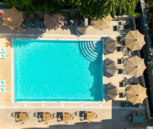 Kuva ulkouima-altaasta, jota ympäröivät aurinkotuolit varjoilla ja pöydät tuoleineen. (Tekoälyn luoma teksti)