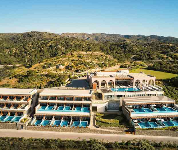 Hotellikompleksi, jossa on useita rakennuksia ja yksityisiä uima-altaita, sijaitsee luonnonkauniilla alueella vuorten ja kasvillisuuden keskellä. (Tekoälyn luoma teksti)