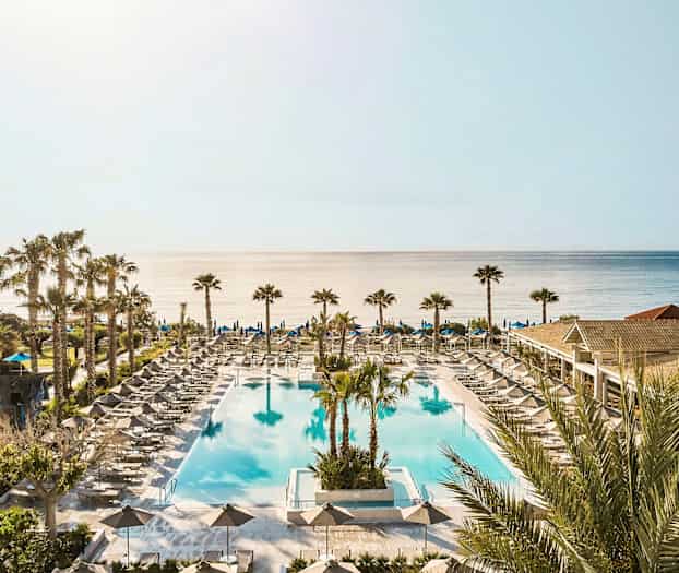 Suuri ulkouima-allas, jonka ympärillä on aurinkotuoleja ja varjoja; taustalla meri. (Tekoälyn luoma teksti)