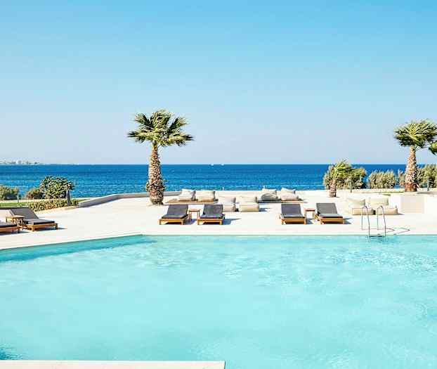 Uima-allasalue meren rannalla, jossa aurinkotuoleja ja palmuja. (Tekoälyn luoma teksti)