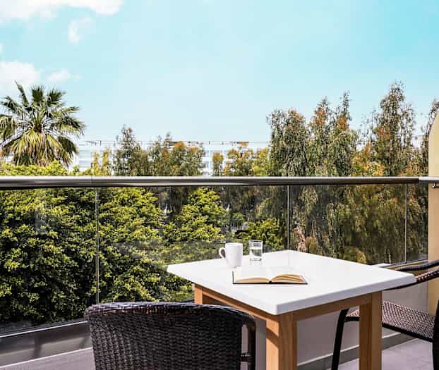 Parveke, jossa on pöytä ja tuolit, näkymä puihin ja taivaalle. (Tekoälyn luoma teksti)