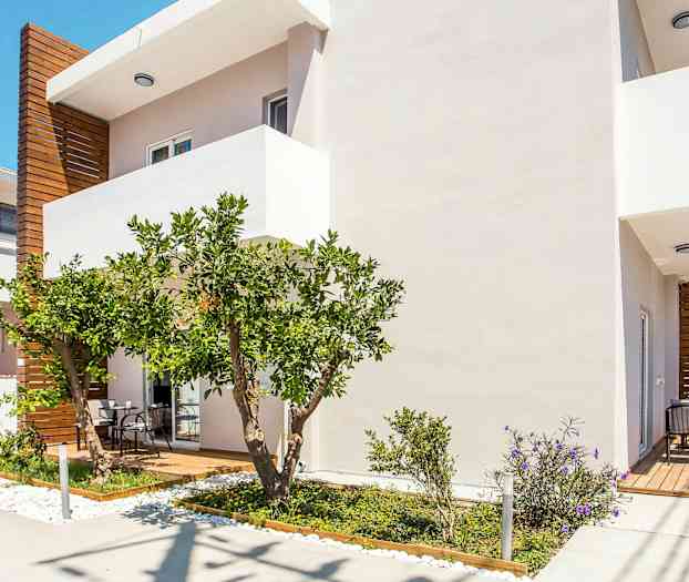 Valkoinen rakennus, jossa on puuyksityiskohtia, terassi ja vehreä puutarha. (Tekoälyn luoma teksti)