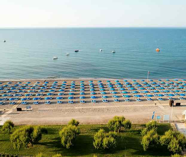 Ranta, jossa on sinisiä aurinkovarjoja ja aurinkotuoleja rivissä. (Tekoälyn luoma teksti)