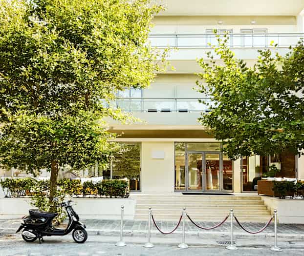 Rakennus, jonka edessä on puita ja pysäköity skootteri sisäänkäynnin edessä. (Tekoälyn luoma teksti)