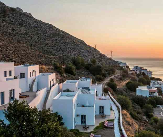 Valkoisiksi maalatut talot rinteessä auringonlaskun aikaan, näkymä merelle. (Tekoälyn luoma teksti)