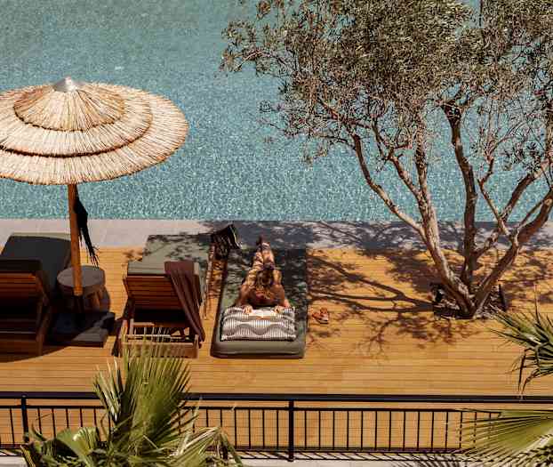 Henkilö makaa aurinkotuolilla altaan vieressä, ympärillä puita ja varjoja. (Tekoälyn luoma teksti)