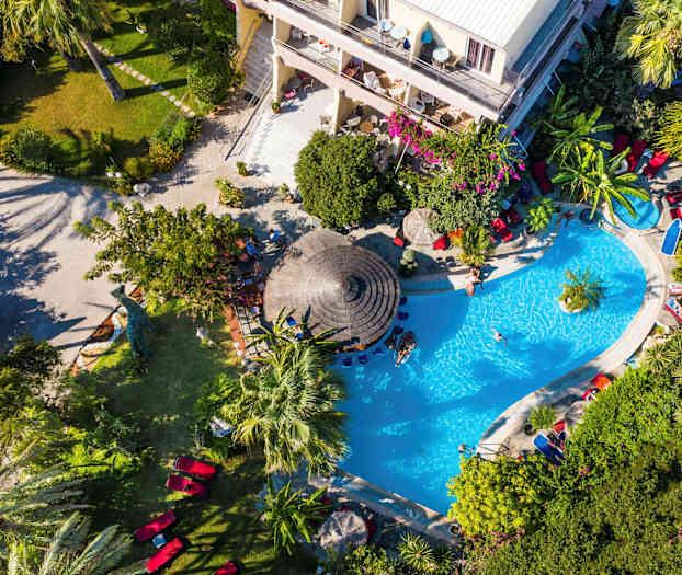 Näköala ylhäältä uima-allasalueelle, jota ympäröi vehreys ja hotelli. (Tekoälyn luoma teksti)