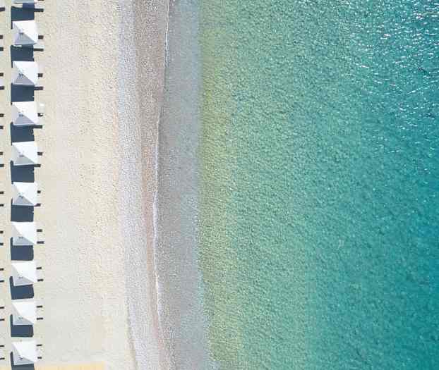 Ilmakuva rannasta, jossa on aurinkovarjoja ja kirkasta turkoosinväristä vettä. (Tekoälyn luoma teksti)