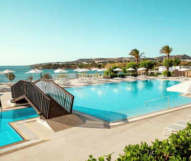 Suuri uima-allas aurinkotuoleilla ja aurinkovarjoilla, näkymä merelle ja vehreään ympäristöön. (Tekoälyn luoma teksti)