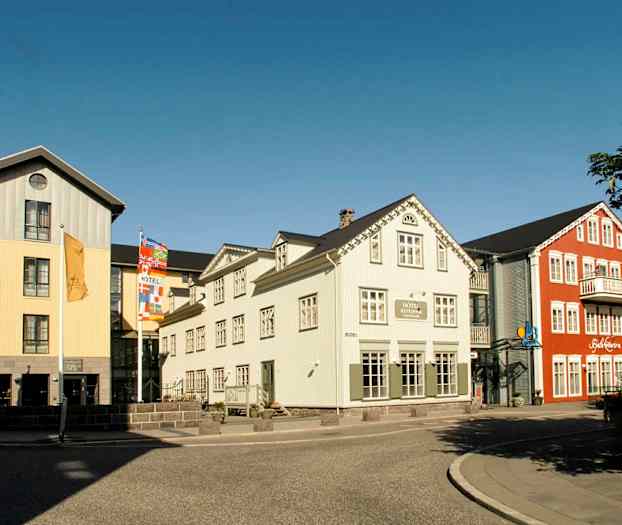 Kuva värikkäistä rakennuksista, joissa hotelli ja ravintola kadun lähellä olevalla jalkakäytävällä. (Tekoälyn luoma teksti)