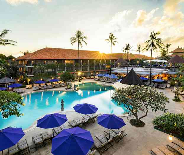 Kuva lomakohteesta, jossa on uima-allas, ympäröivä aurinkotuoleja ja aurinkovarjoja sekä taustalla vihreitä palmuja. (Tekoälyn luoma teksti)