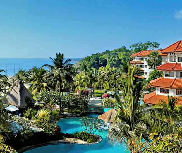 Kuva trooppisesta lomakohteesta, jossa on uima-allas, palmuja ja punakattoisia rakennuksia meren lähellä. (Tekoälyn luoma teksti)