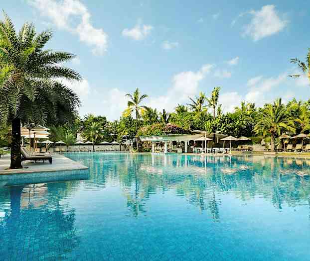 Suuri uima-allas, jota ympäröivät aurinkotuolit, aurinkovarjot ja palmut, taustalla kirkas sininen taivas. (Tekoälyn luoma teksti)