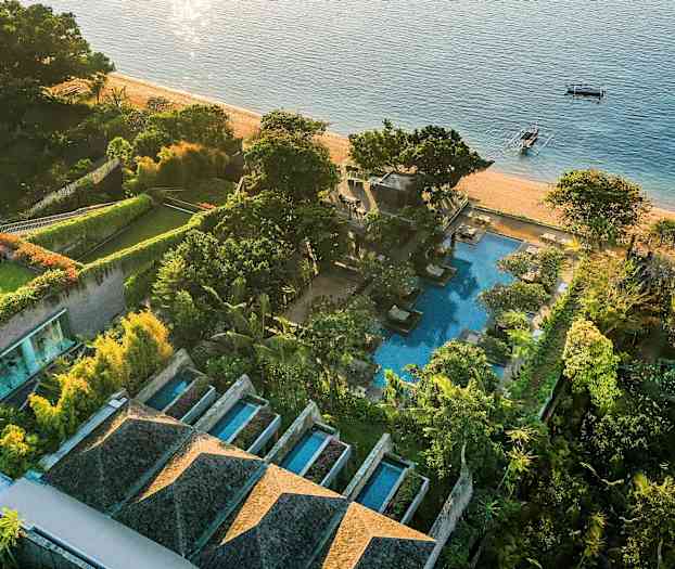 Linnunäkymä rantaläheisestä luksushotellista, jossa on uima-altaita, vihreitä puutarhoja ja rannalla rajoittuva meri. (Tekoälyn luoma teksti)