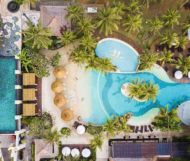 Ilmakuva altaasta aurinkotuoleineen, varjoineen ja rehevine palmuineen. (Tekoälyn luoma teksti)