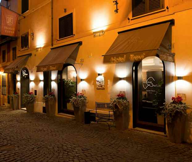 Hotellin sisäänkäynti, jossa kutsuva valaistus, kukkaruukut ja kyltit. (Tekoälyn luoma teksti)