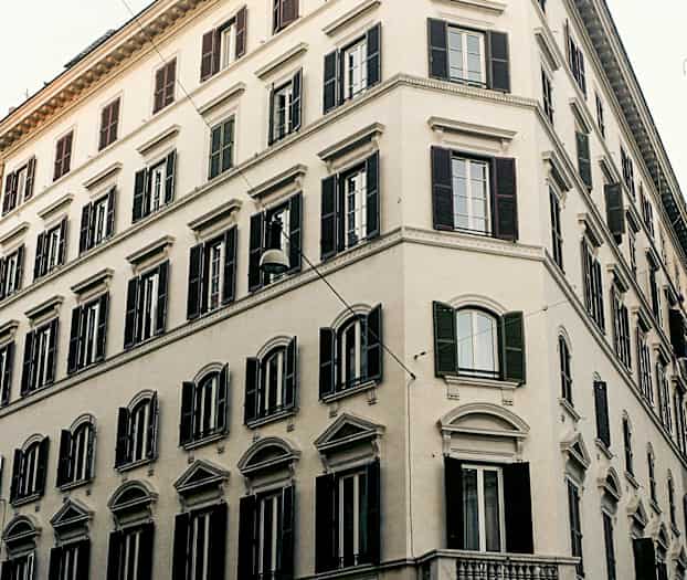 Kulmarakennus, jossa on klassista arkkitehtuuria ja tummia ikkunaluukkuja. (Tekoälyn luoma teksti)