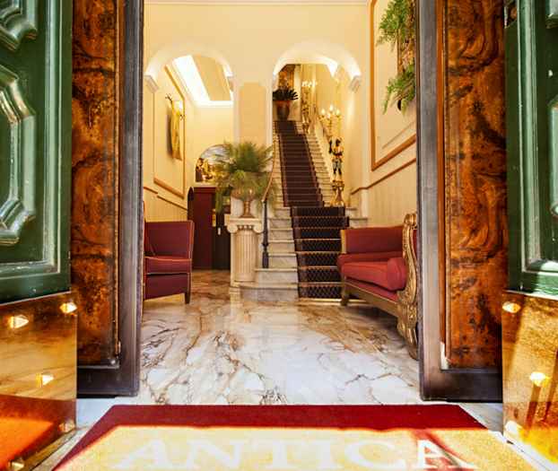 Tyylikkään hotellin sisäänkäynti marmorialustalla, punaisilla tuoleilla ja portaikkoa. (Tekoälyn luoma teksti)