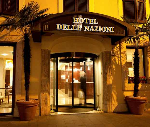 Hotel delle Nationin sisäänkäynti lasiovilla ja valaistuksella illalla. (Tekoälyn luoma teksti)