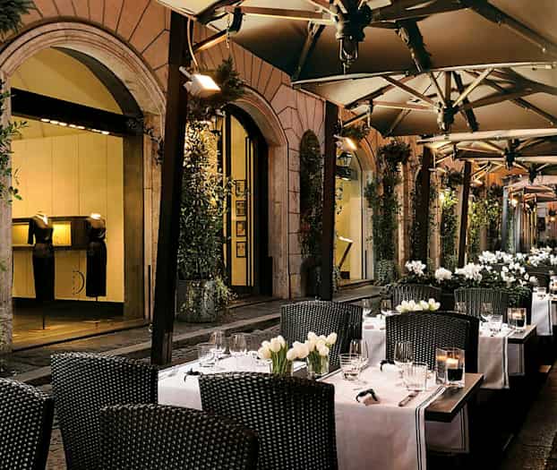 Ulkoilmaravintola, jossa pöytiä, valkoiset pöytäliinat ja kukkakoristeita. (Tekoälyn luoma teksti)